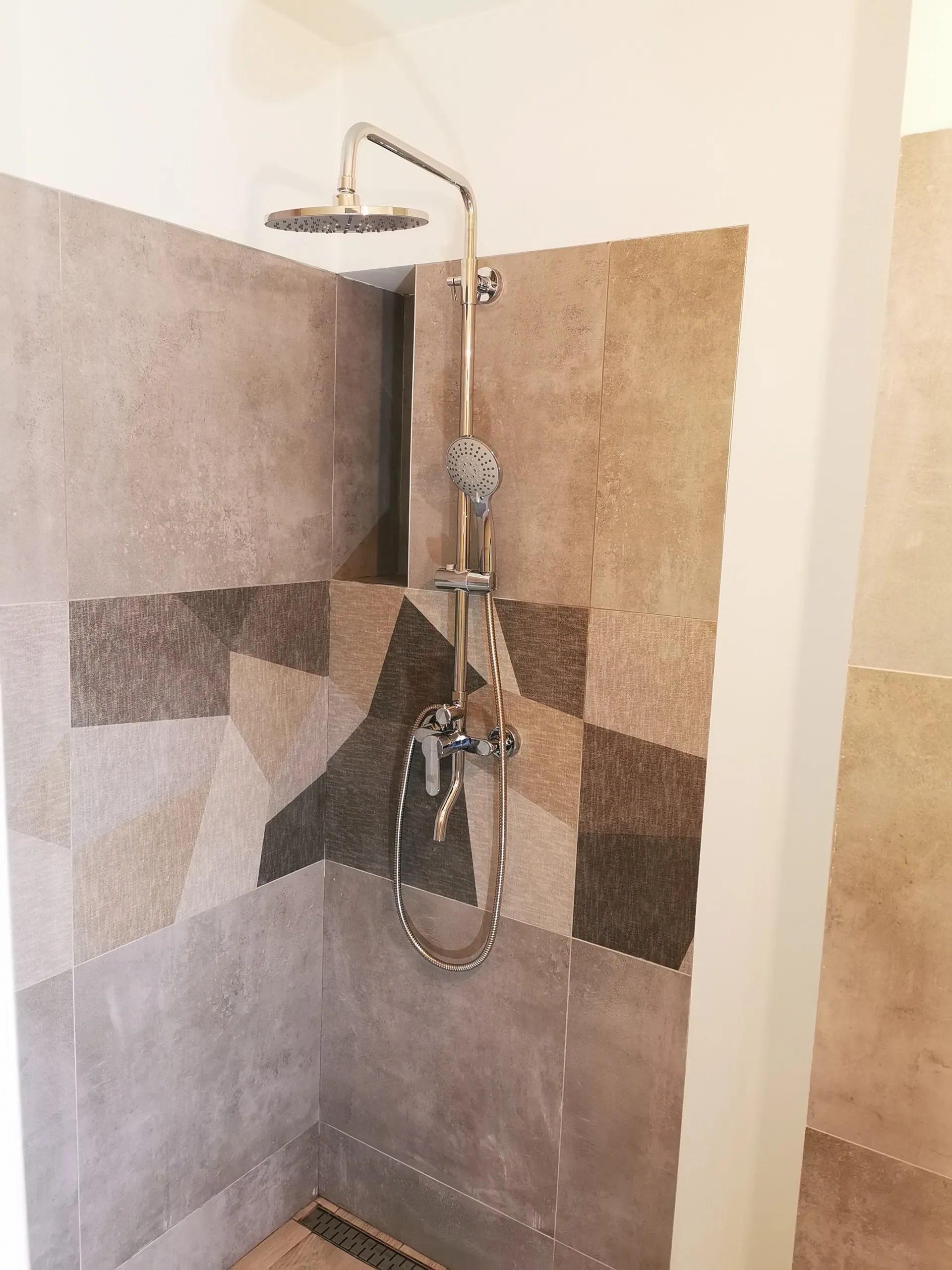 Gotowa wnęka prysznicowa z deszczownicą i pasem dekoracyjnych płytek w geometryczny patchwork.